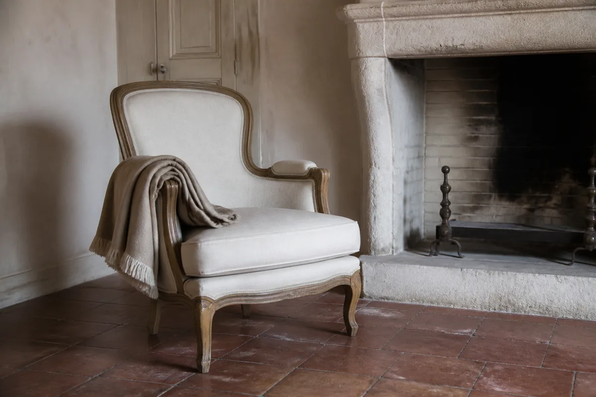 Fauteuil ancien et plaid de laine près d&rsquo;une cheminée éteinte dans un gîte français